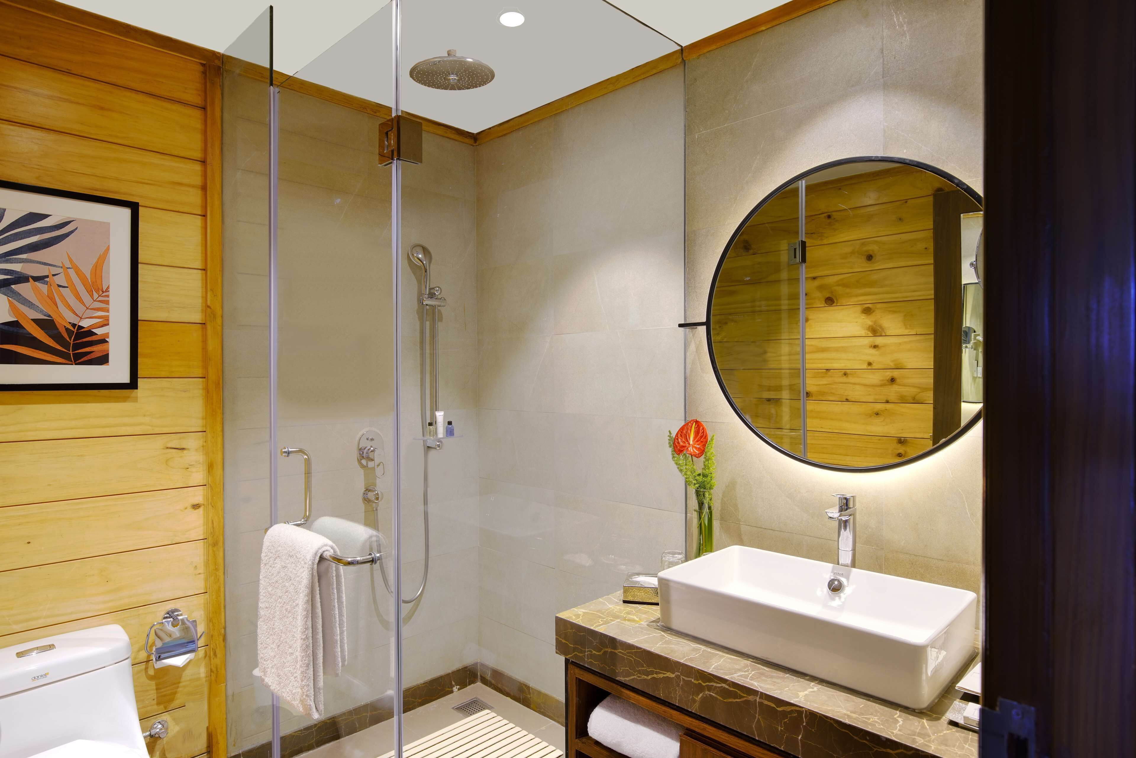 A modern bathroom with a glass-enclosed shower, a wooden vanity with a marble countertop, and a large mirror.