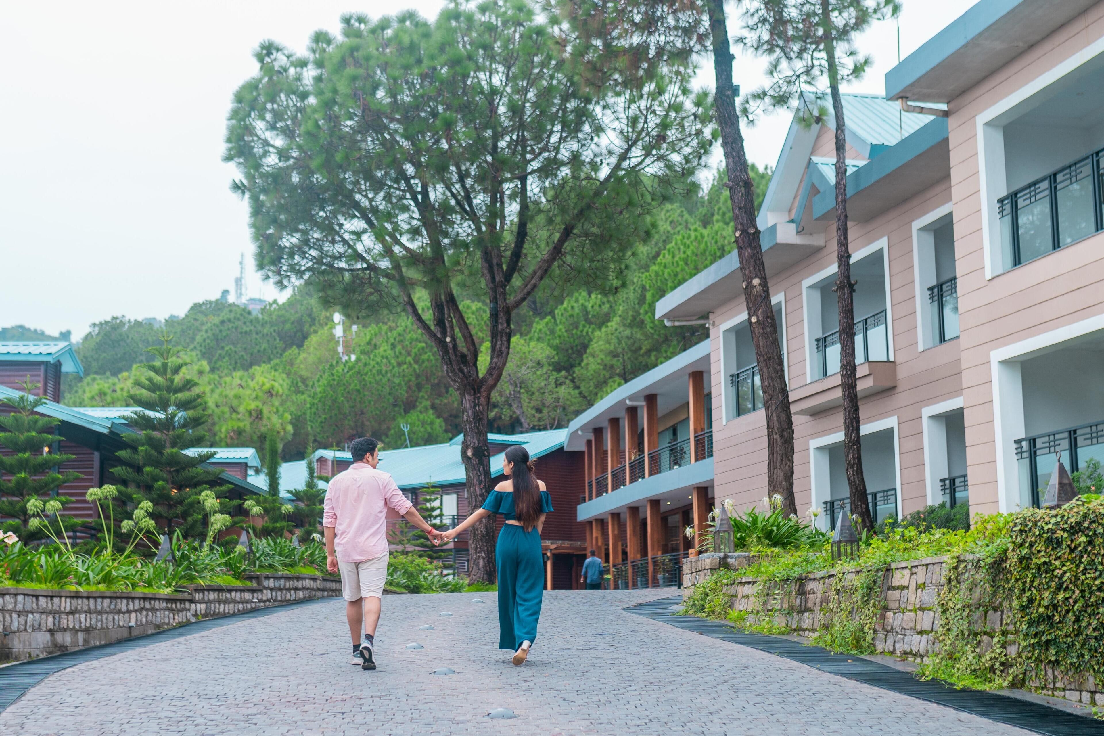 A couple walking on a paved pathway in a resort area with buildings and trees.