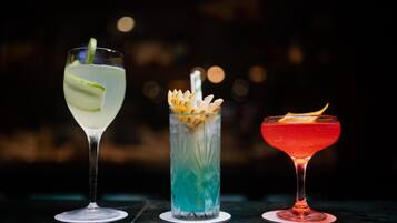 Drei verschiedene Cocktails in Gläsern auf einem Tisch vor dunklem Hintergrund.