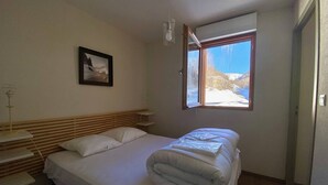 A bedroom with a bed, a bedside table, a lamp, a window with a view of snow-covered mountains, and a framed picture on the wall.