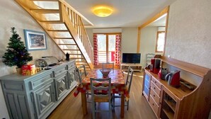 A cozy dining area with a wooden staircase, a small Christmas tree, and a TV in the background.