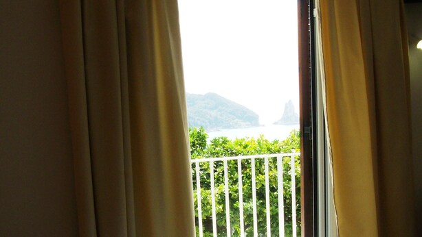 Quarto de hotel com cama, vista para uma varanda com grades e janela com cortinas.