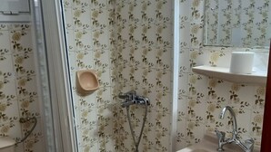 Casa de banho com chuveiro, sanita, lavatório e espelho.
