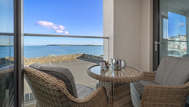 A balcony with wicker furniture, a glass table, and a view of the sea.