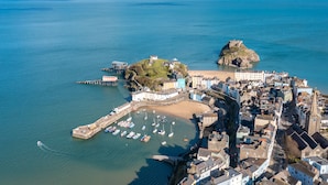 An aerial view of a coastal town with a historic fort, a harbor with boats, and a mix of residential and commercial buildings.