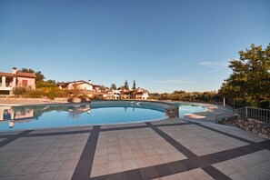 A swimming pool with a tiled deck, surrounded by buildings and trees.