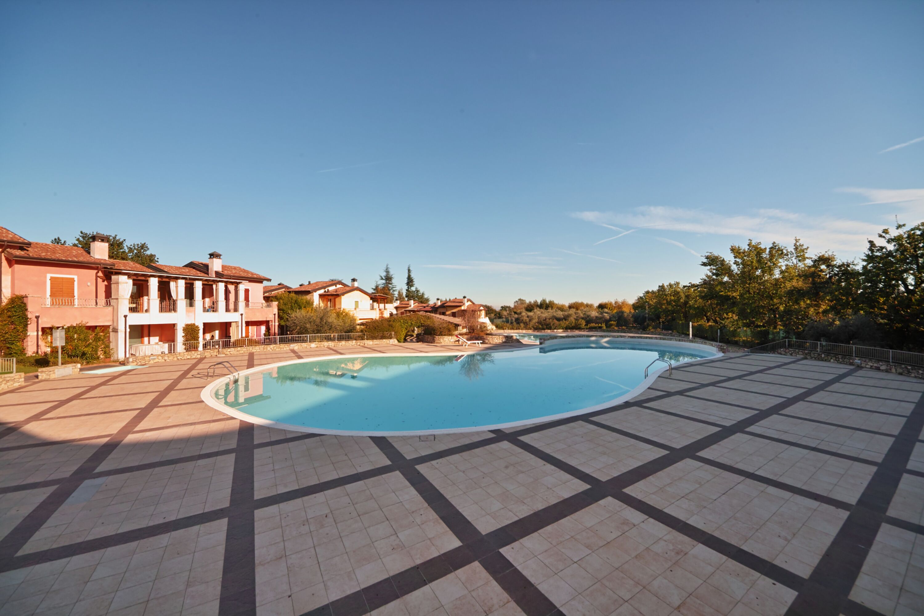 A large swimming pool with a tiled deck, surrounded by buildings with balconies and a clear sky.