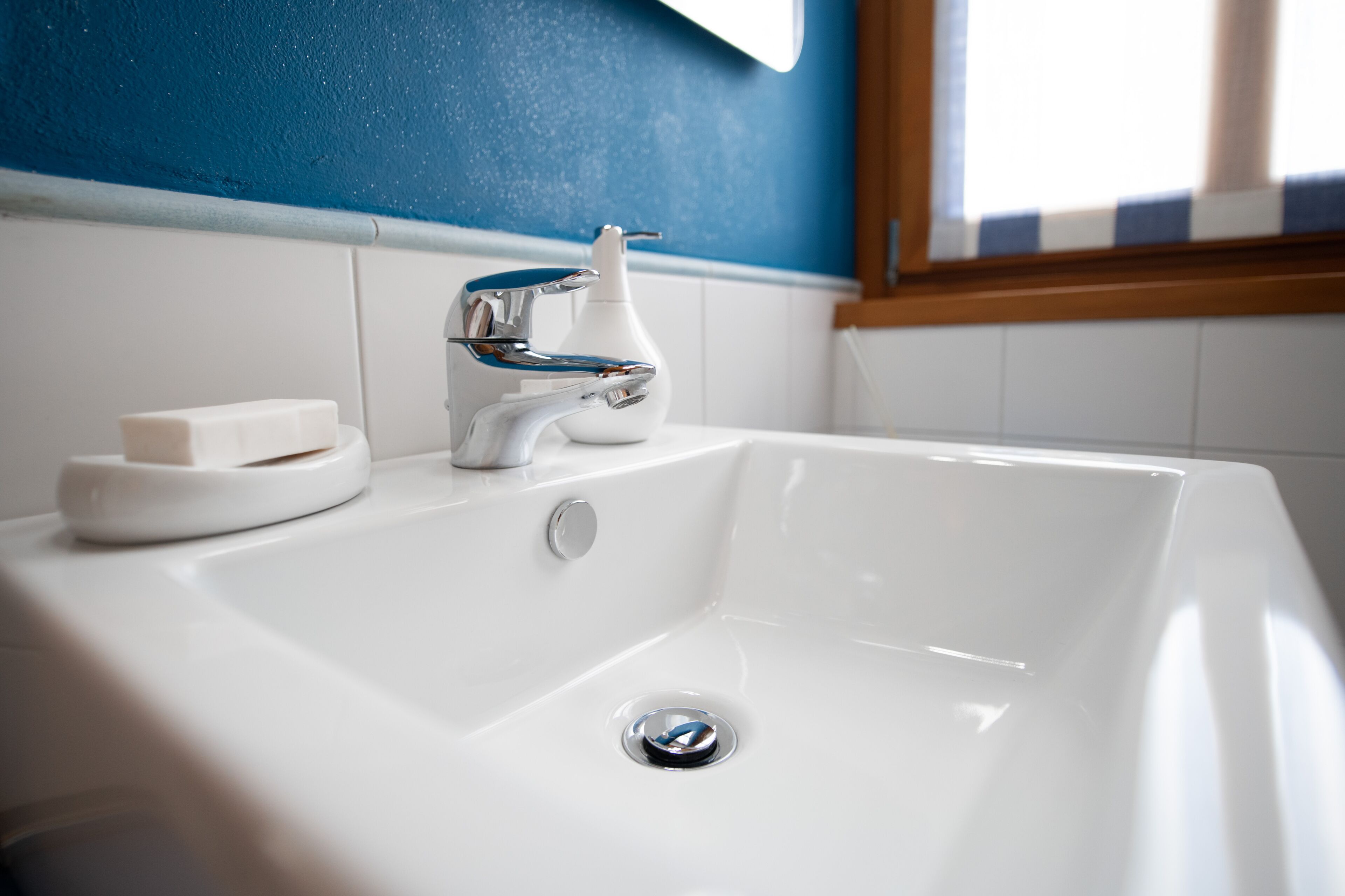 A white bathroom sink with a chrome faucet, soap dish, and a window above.