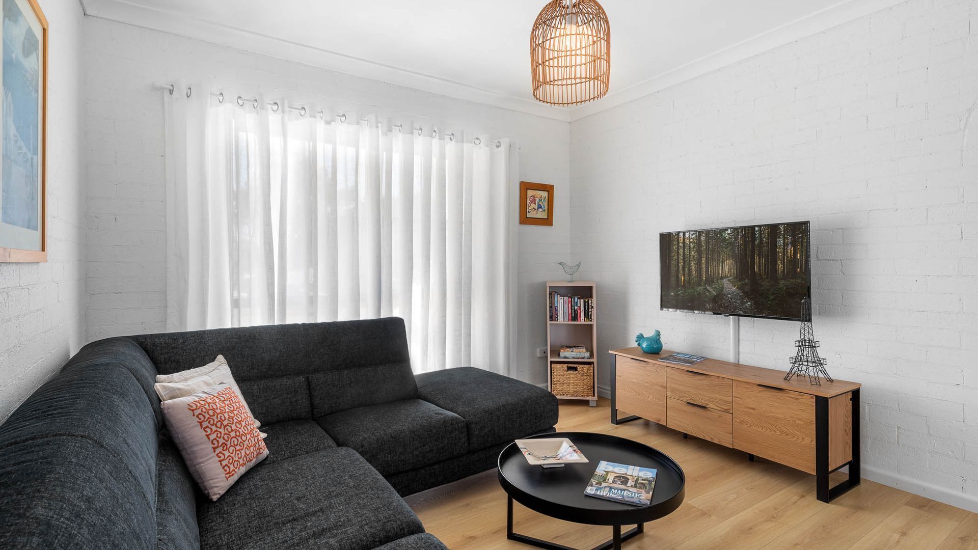 A modern living room with a grey sectional sofa, a black coffee table, a wooden TV stand, and a large flat-screen TV.