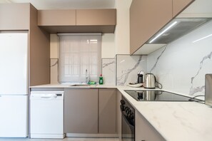 A modern kitchen with a built-in dishwasher, a stainless steel kettle, and a marble backsplash.