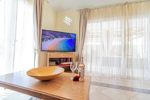 A living room with a flat-screen TV, a wooden table with a bowl and wine glasses, and a bookshelf.