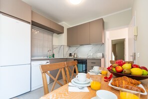 Une cuisine moderne avec une table à manger dressée pour le petit-déjeuner, comprenant des fruits, des croissants et un verre de jus d’orange.