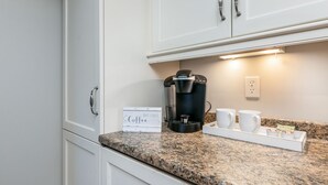 A kitchen with white cabinets, a Keurig coffee maker, two white mugs, and a tray with coffee pods. - Walk to Town, Riverfront Retreat & Beach Pass (Kennebunk)