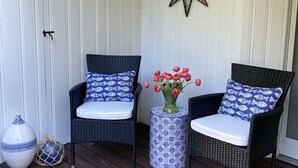 A porch with two wicker chairs, a decorative star, and a vase with flowers. - Walk to Town, Riverfront Retreat & Beach Pass (Kennebunk)
