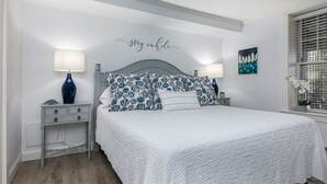 A bedroom with a bed, two bedside tables, a wall-mounted artwork, and a window with blinds. - Walk to Town, Riverfront Retreat & Beach Pass (Kennebunk)