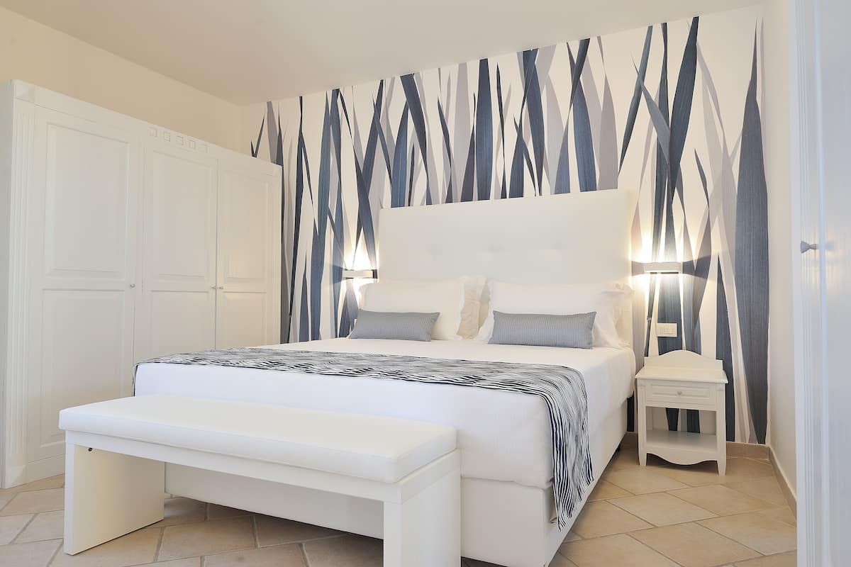 A bedroom with a large bed, bedside tables, a bench, and a wall with a geometric pattern.
