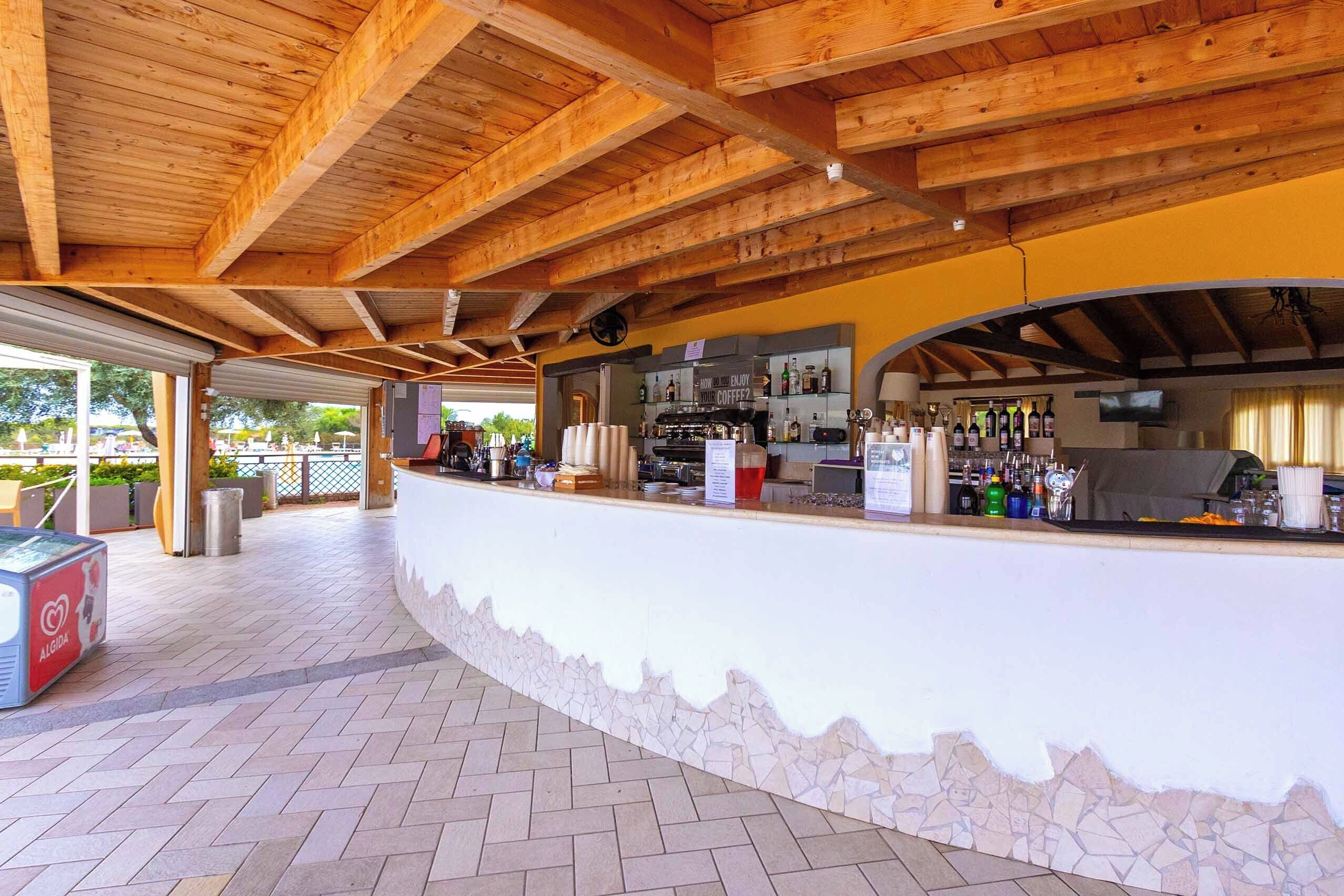 Un área de bar al aire libre con mostrador de piedra, vigas de techo de madera y suelo de baldosas.