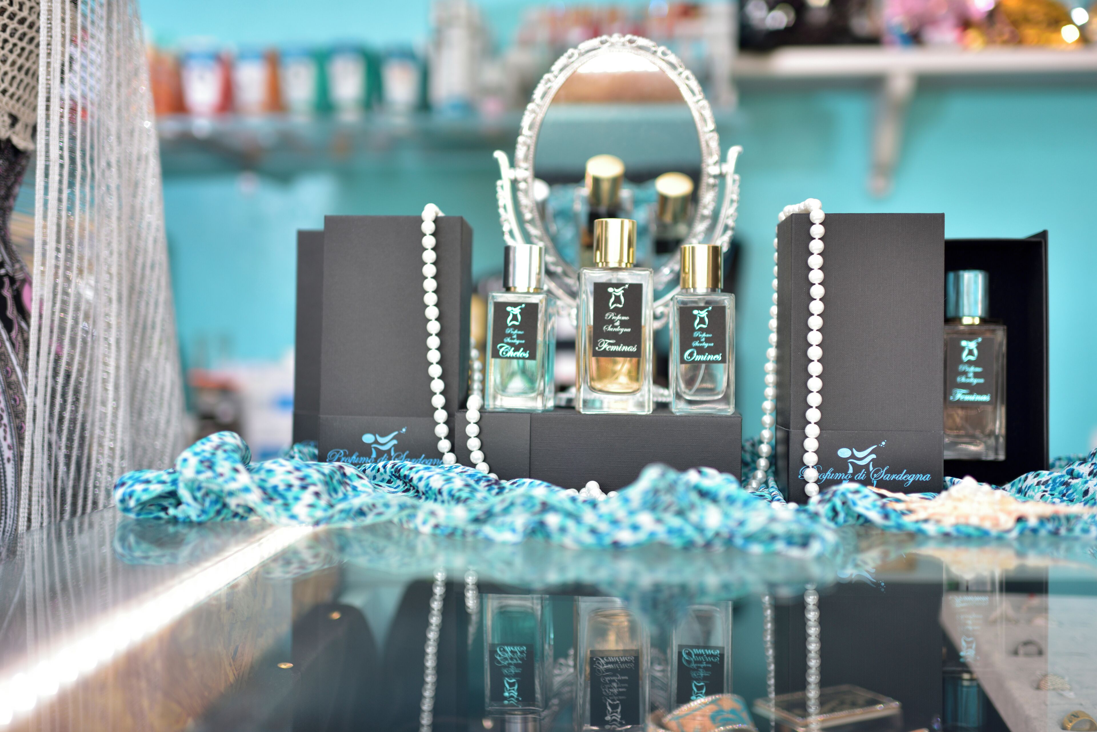 A display of perfume bottles in black boxes with pearl chains, set on a reflective surface with a blue and white patterned cloth underneath.