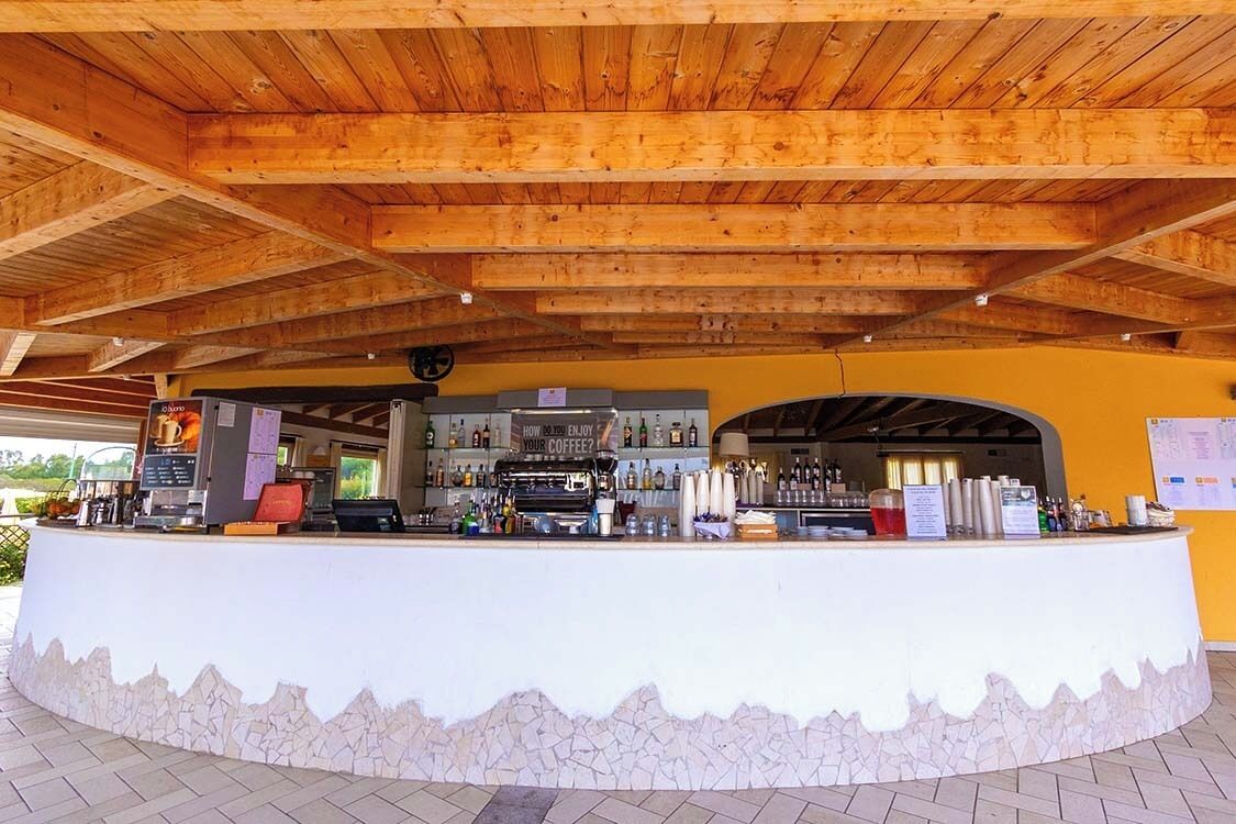 A bar area with a stone base and wooden ceiling, featuring a counter with various beverages and a coffee machine.