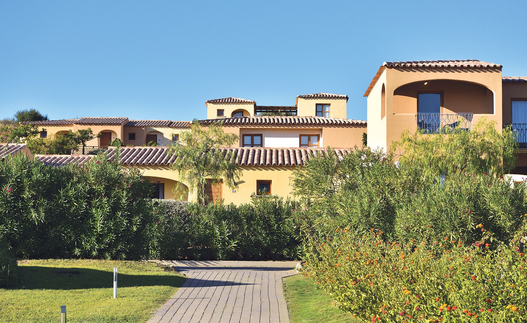 A hotel with multiple buildings, a paved walkway, and lush greenery.