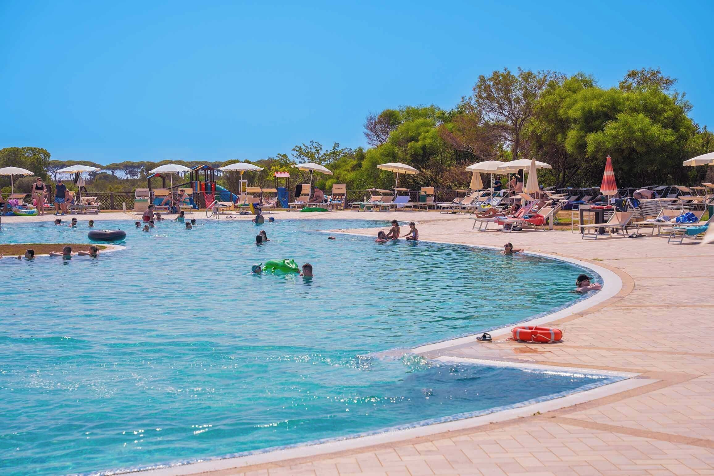 Una amplia piscina al aire libre con varias pistas de natación, rodeada de tumbonas y sombrillas.
