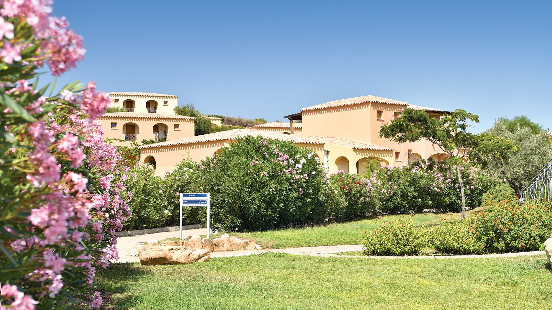 A hotel with multiple buildings, a well-maintained garden, and a clear blue sky.