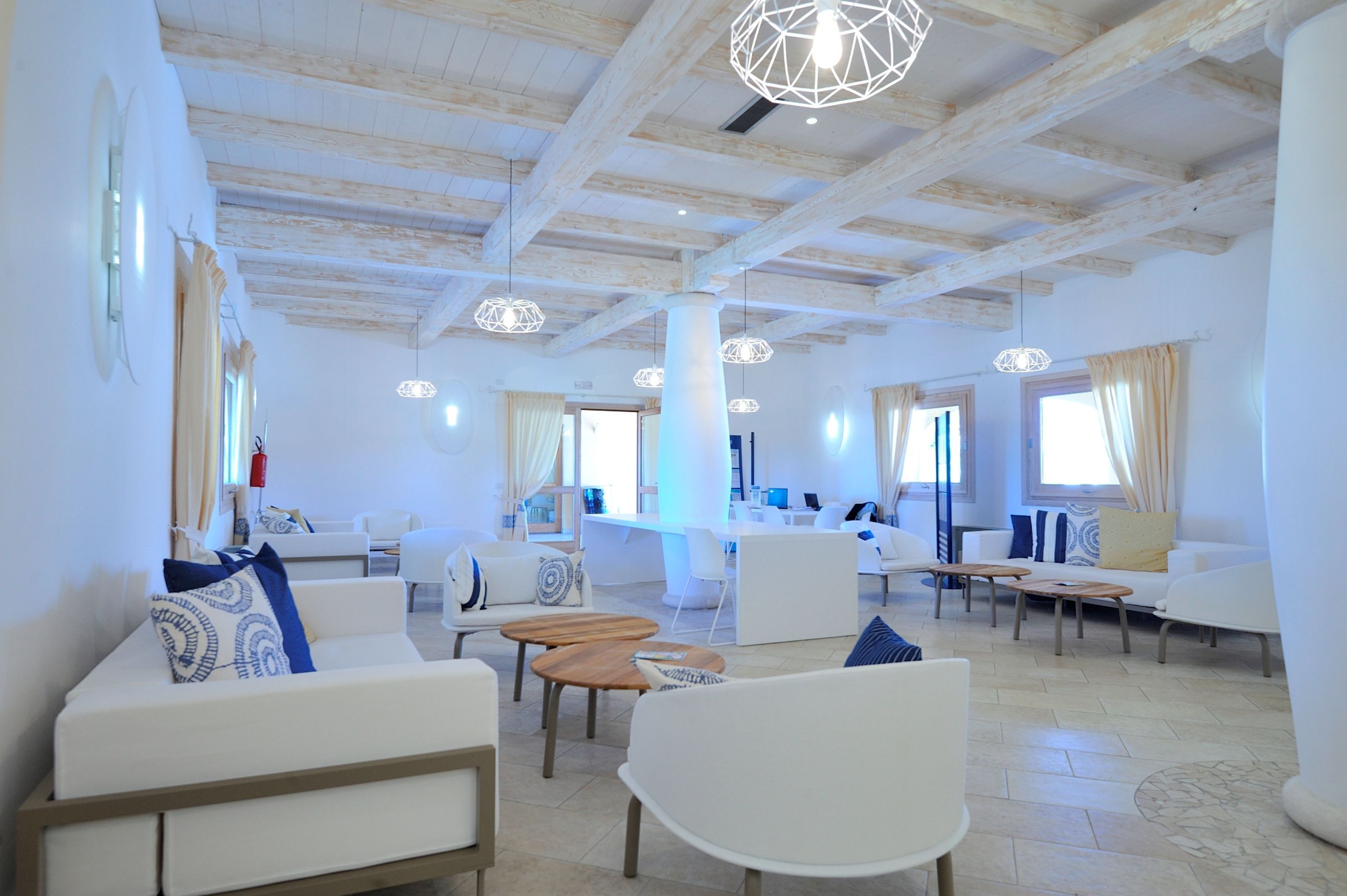 A spacious, well-lit living area with white furniture, wooden tables, and hanging pendant lights.