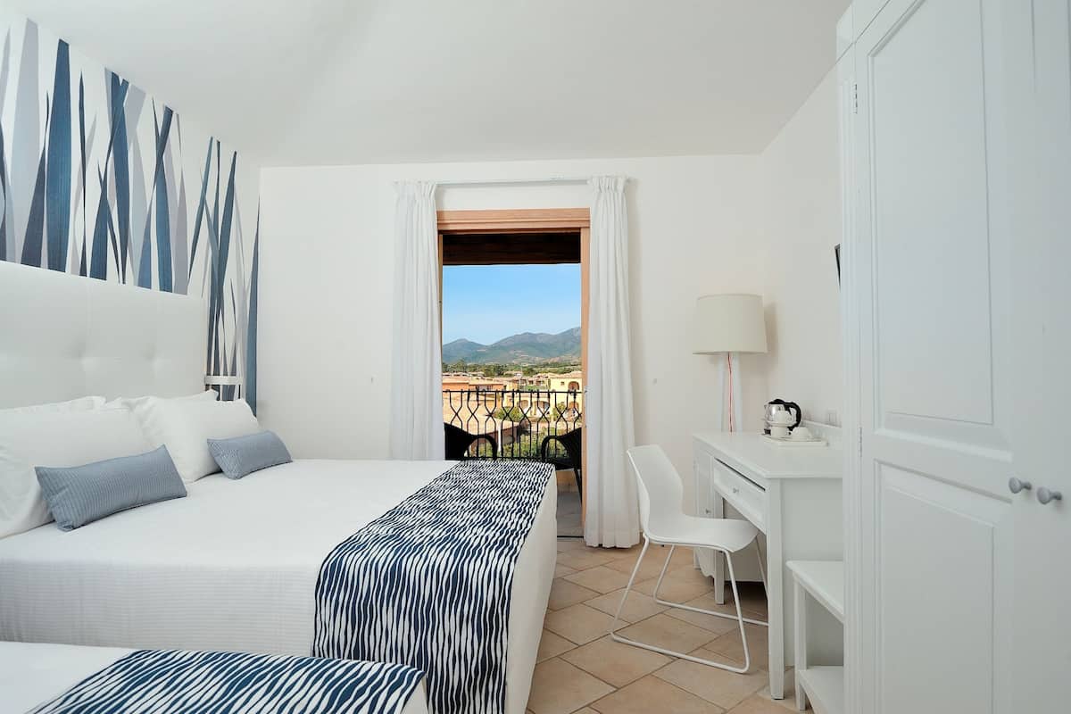 A hotel room with a bed, a desk, a chair, and a view of the mountains.
