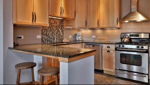 Una cocina moderna con armarios de madera, encimera de granito, electrodomésticos de acero inoxidable y una isla integrada con taburetes.