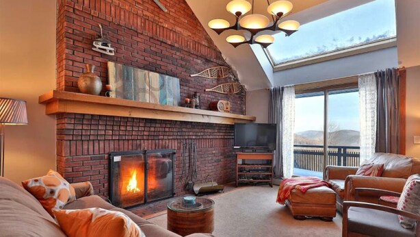 Una sala de estar acogedora con chimenea de ladrillo, asientos cómodos y un amplio ventanal con vistas al exterior.