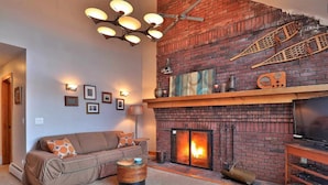 Una sala de estar acogedora con una chimenea de ladrillo, un sofá, una mesa de centro y un televisor.