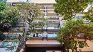 Un edificio de varios pisos con balcones, un acceso cubierto y árboles en primer plano.