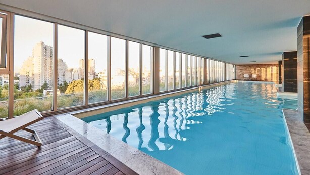 Una piscina interior larga con vistas a un paisaje urbano a través de amplios ventanales.