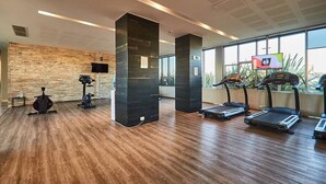 Un gimnasio moderno con suelo de madera, equipamiento de ejercicio, ventanas amplias y una pared de piedra.