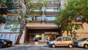 Un edificio de varios pisos con un diseño arquitectónico moderno, con balcones y una entrada empedrada con ladrillos.