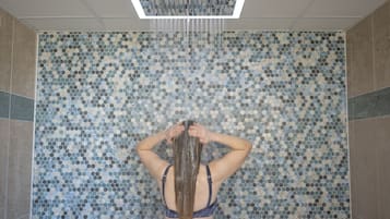 Experience the unique mosaic tile wall in this shower area, featuring a ceiling-mounted showerhead and a textured design.