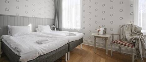 A neatly made bed with white linens, a grey headboard, and a small round table with a bottle and glasses.
