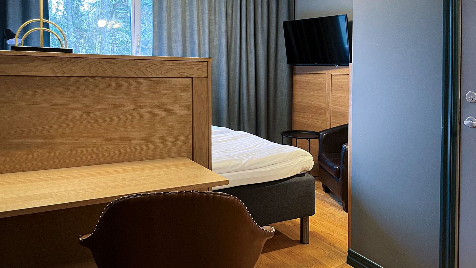 Una habitación de hotel moderna con un escritorio de madera, una cama, un televisor y una silla.