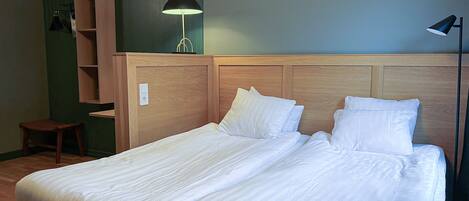 A neatly made bed with white linens, a wooden headboard, and a bedside lamp.