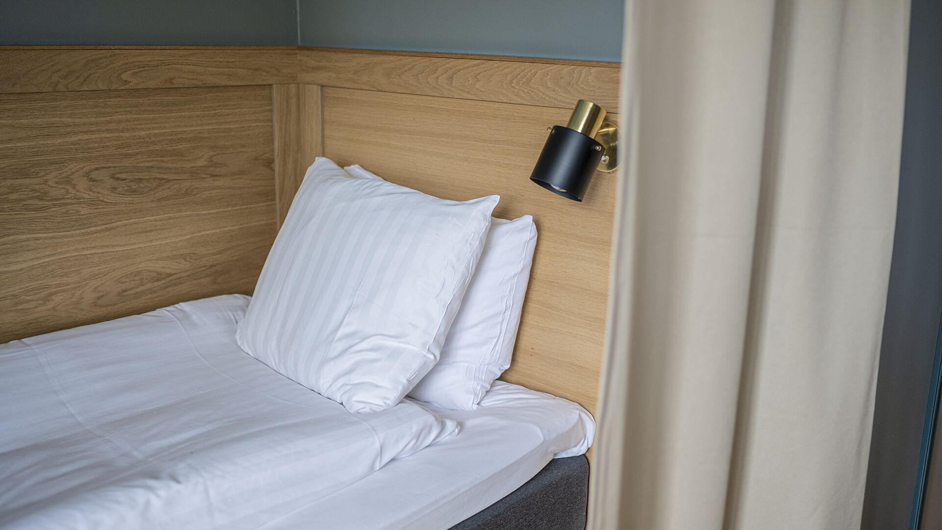 Un lit bien fait, avec du linge de lit blanc et des oreillers, une tête de lit en bois et un luminaire fixé au mur.