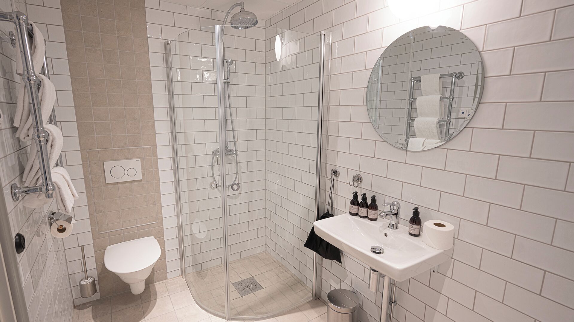 A modern bathroom with a glass-enclosed shower, a white toilet, and a sink with toiletries.