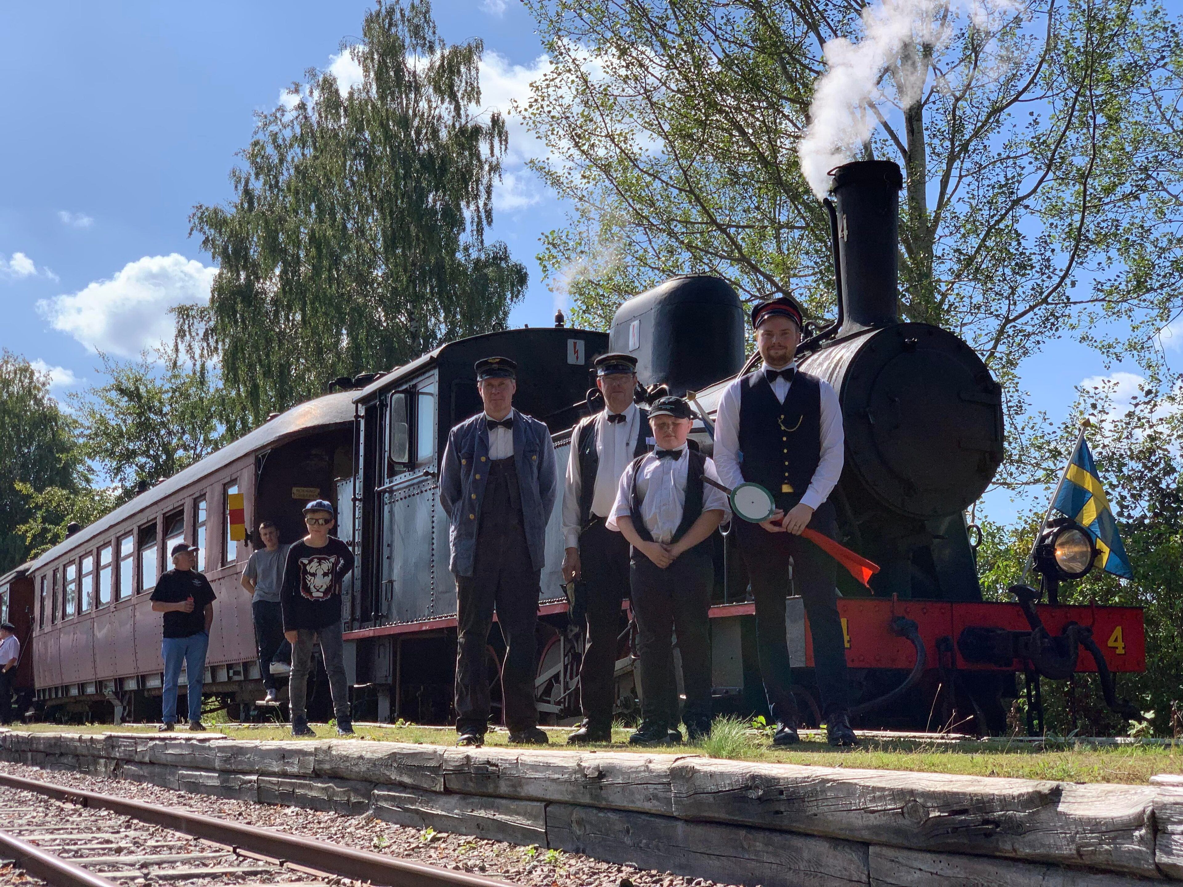 A vintage steam locomotive with a group of men in period attire standing beside it.