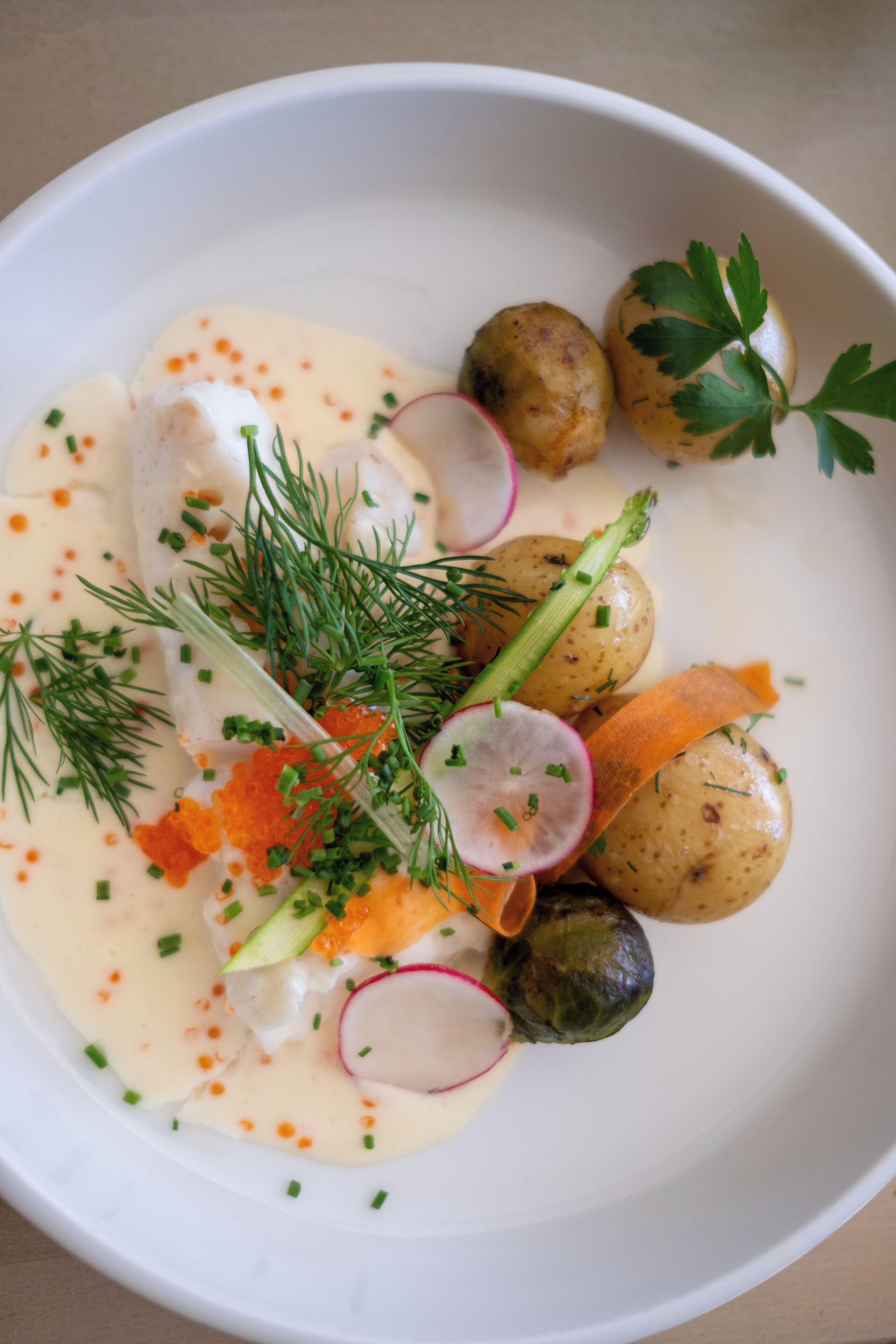 Une assiette blanche contenant une sauce crémeuse, garnie d’aneth, de ciboulette, de rondelles de radis et d’œufs de saumon.