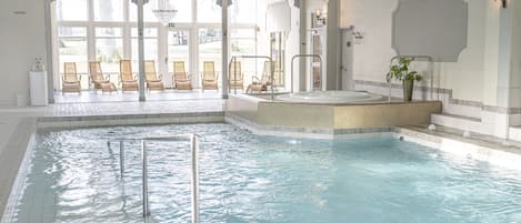 Una piscina interior con hidromasaje, sillas de descanso y vistas al exterior.