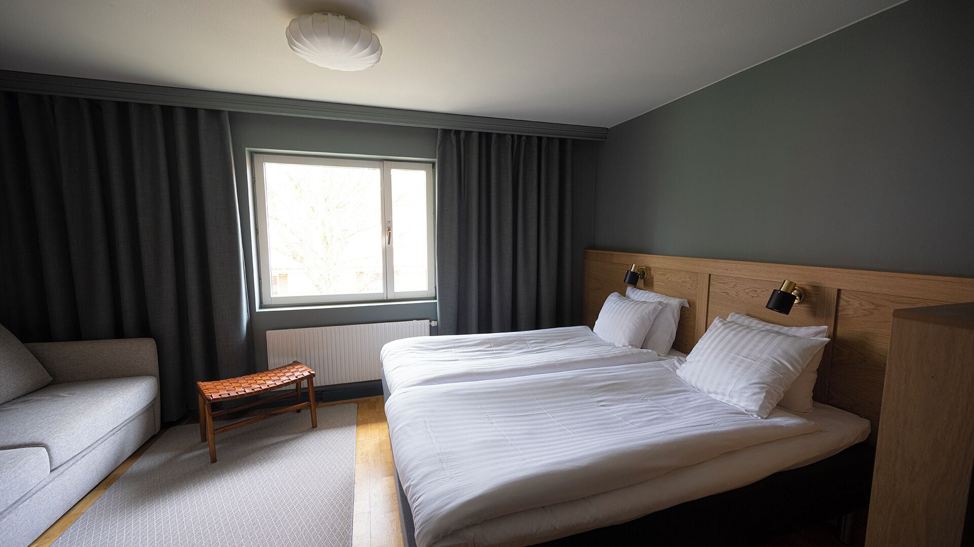 Une chambre d’hôtel avec deux lits, un coin salon, une fenêtre avec des rideaux et un radiateur.