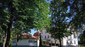 Una fila di edifici bianchi con tetti rossi, immersi nel verde tra alberi e un prato.
