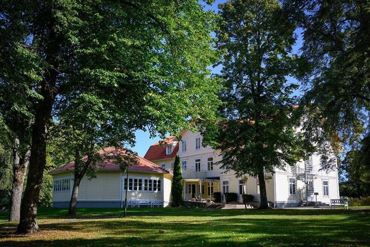 A row of white buildings with red roofs, surrounded by trees and a grassy lawn.