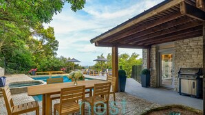 A poolside area with a wooden table and chairs, a barbecue grill, and a stone wall. - ***NEW*** 7 MINUTES TO DOWNTOWN | POOL | HOT TUB | POOL TABLE | FOOSBALL | FIRE PIT | 13 Queen Beds (Austin)
