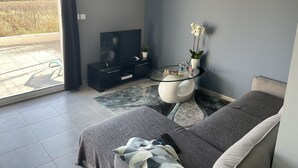 Una sala de estar moderna con un sofá, una mesa de centro de vidrio, un televisor y una planta en maceta.