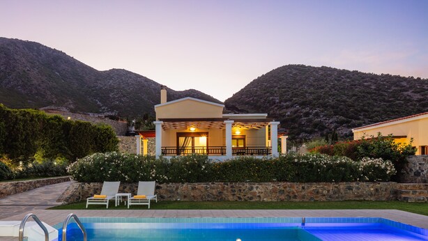 Zona de piscina con una casa al fondo, rodeada de vegetación y montañas.